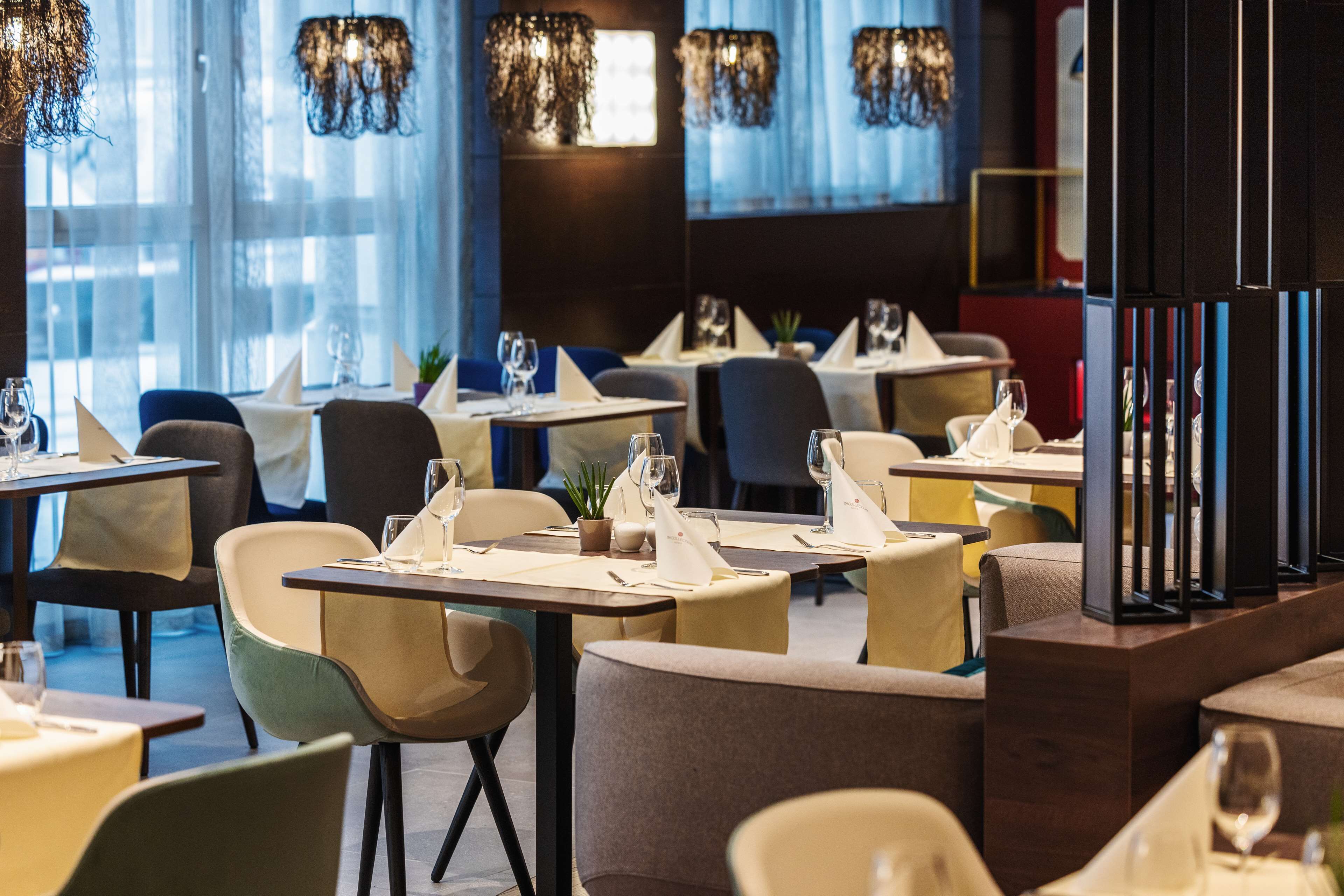 Un interior de restaurante con mesas dispuestas para comer, sillas y lámparas colgantes.