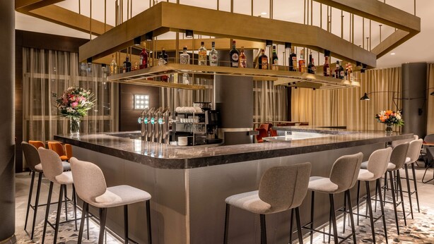 A modern bar area with a central island, bar stools, and a variety of bottles.