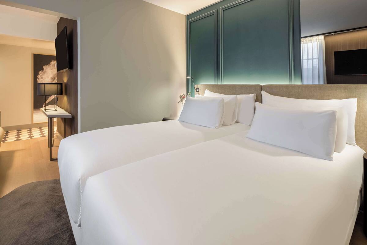 Une chambre d’hôtel avec un grand lit, un téléviseur fixé au mur et une petite table avec une lampe.