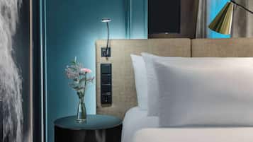 A hotel room with a bed, a bedside table with a vase of flowers, a wall-mounted TV, and a modern lamp.