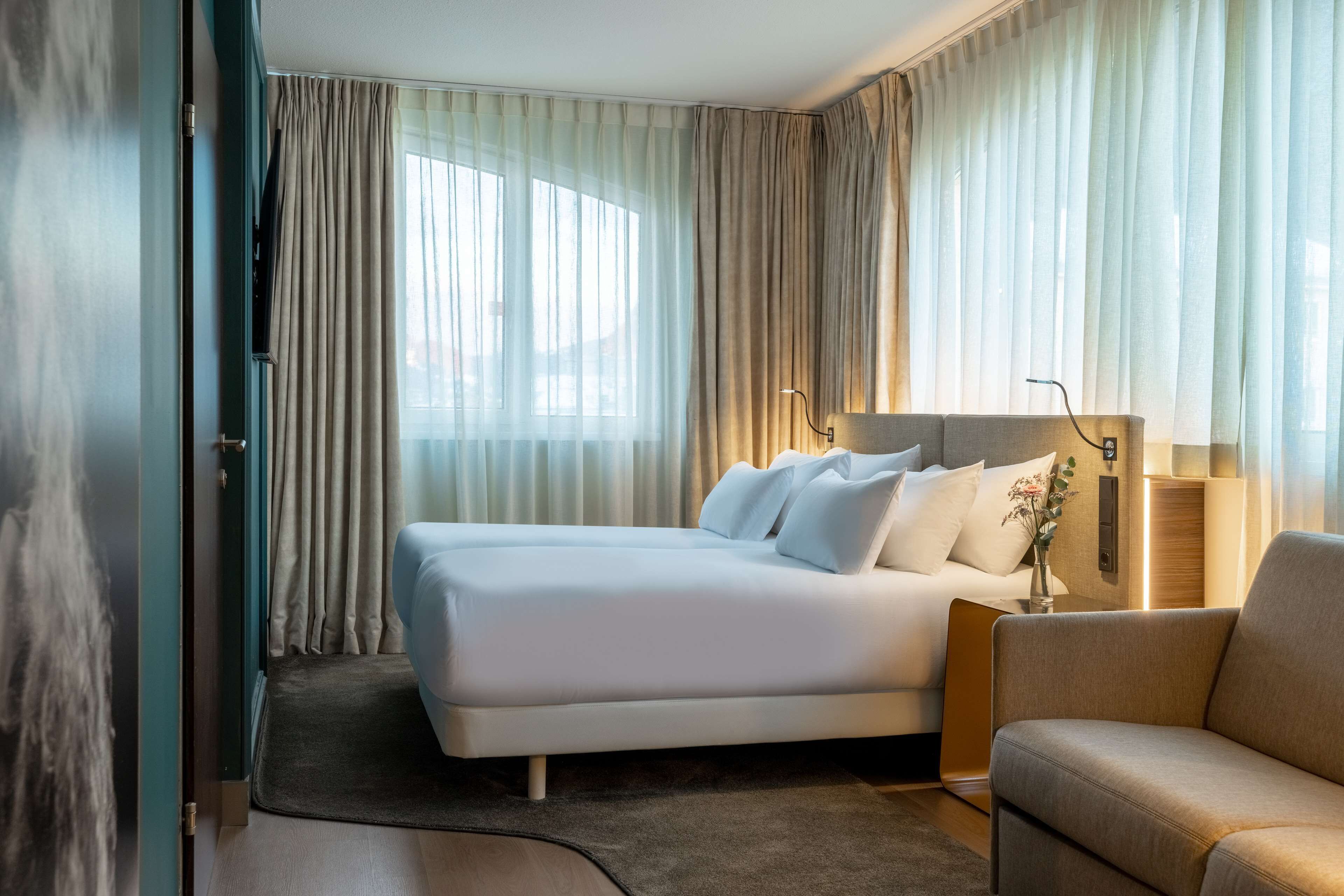 Een hotelkamer met een bed, een bank, een lamp en uitzicht op de omgeving.