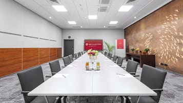 A conference room with a long table, chairs, a red banner, and a decorative wall.