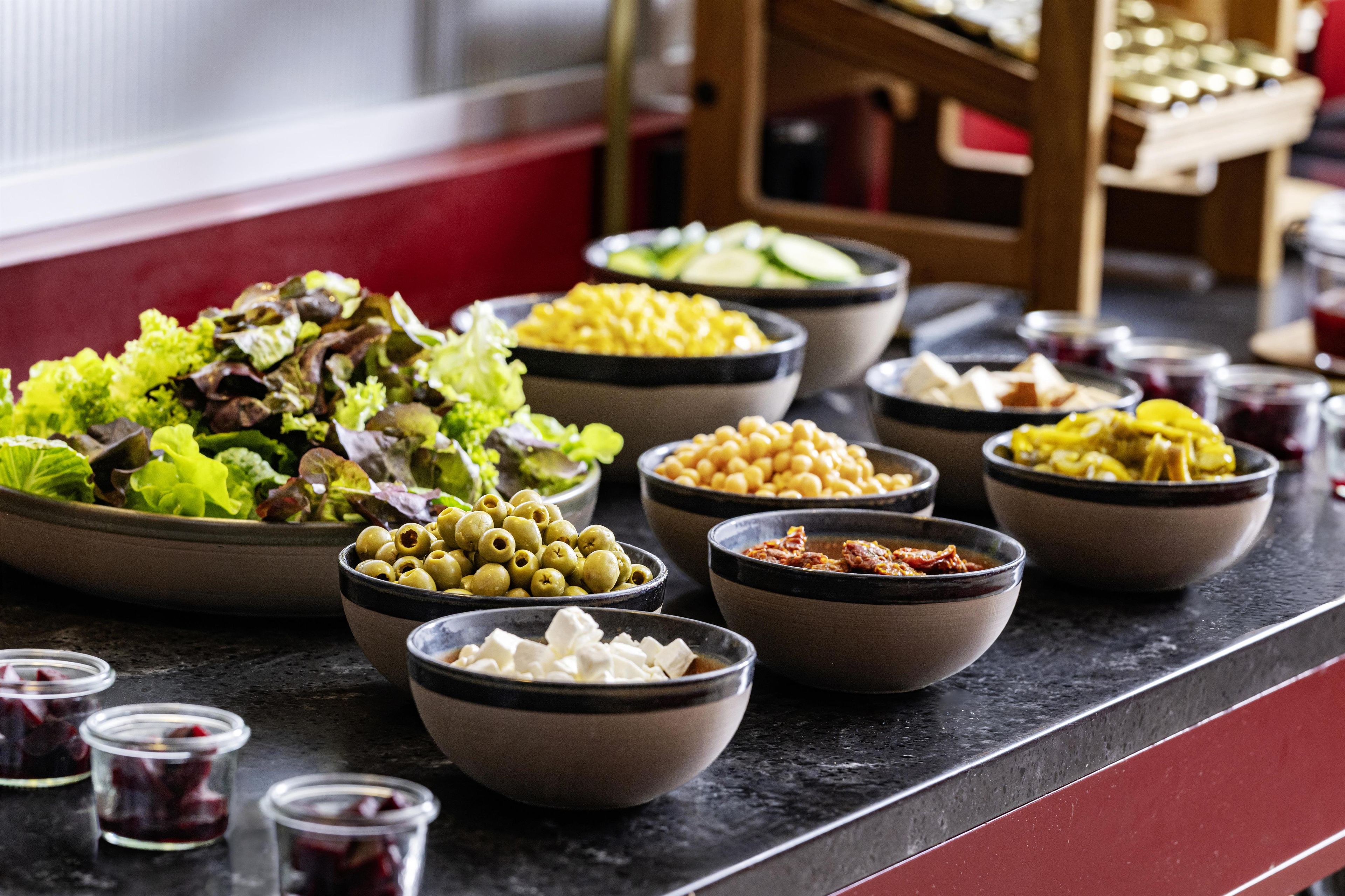 A buffet table with various food items including salads, olives, and other dishes.