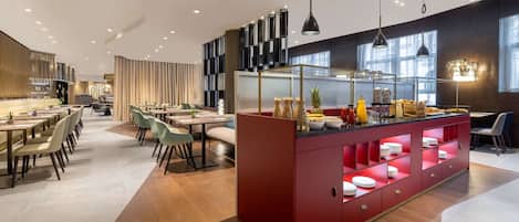 A modern dining area with multiple tables and chairs, a central island with a red base, and a kitchen area with a glass partition.