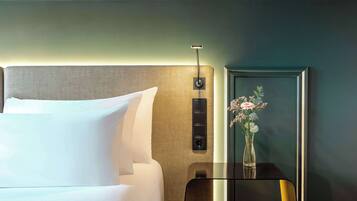 Habitación de hotel con una cama bien hecha, una mesita de noche con un jarrón de flores y un panel de control en la pared.