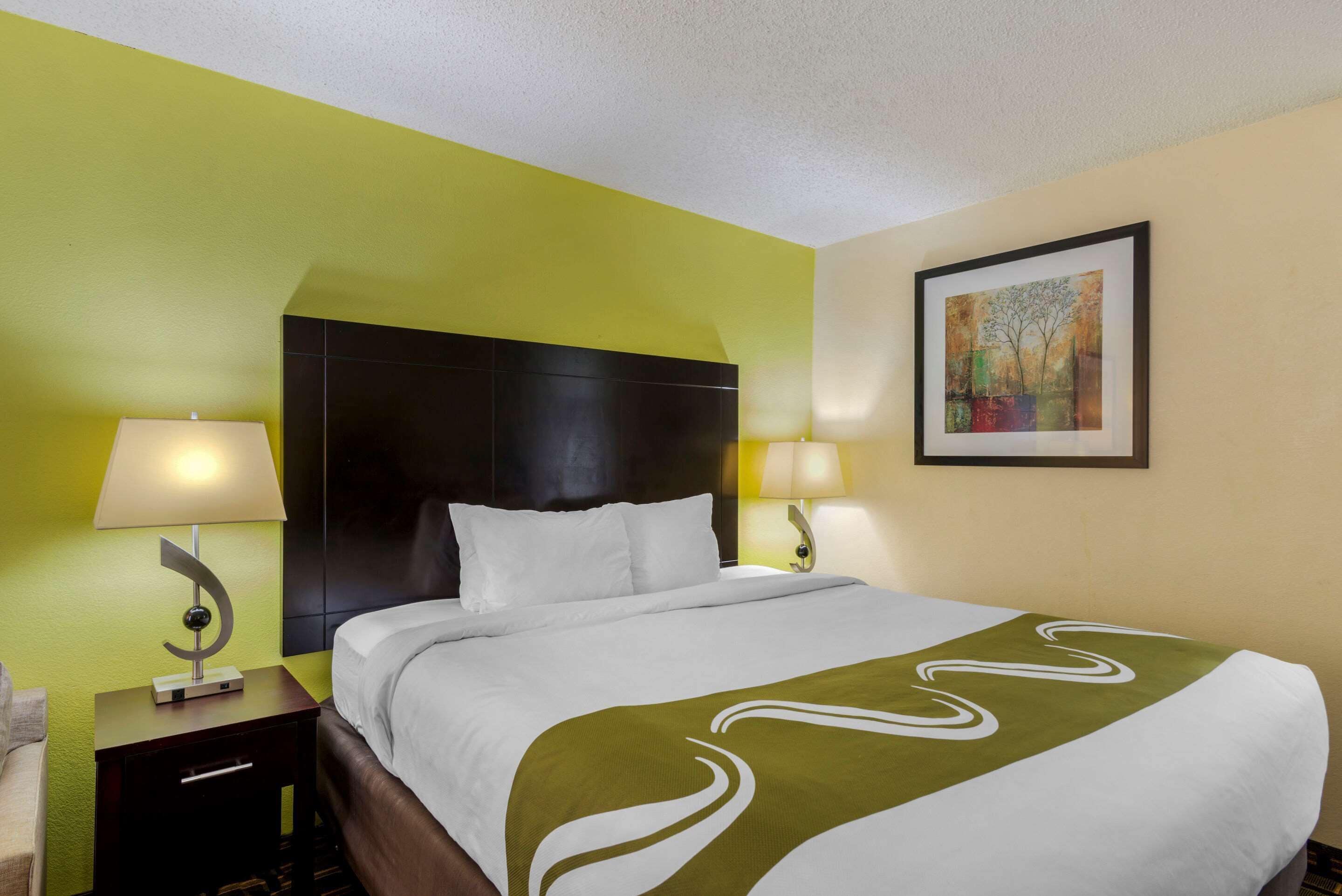 Una habitación de hotel con una cama, dos lámparas de noche, una mesita de noche y un cuadro en la pared.