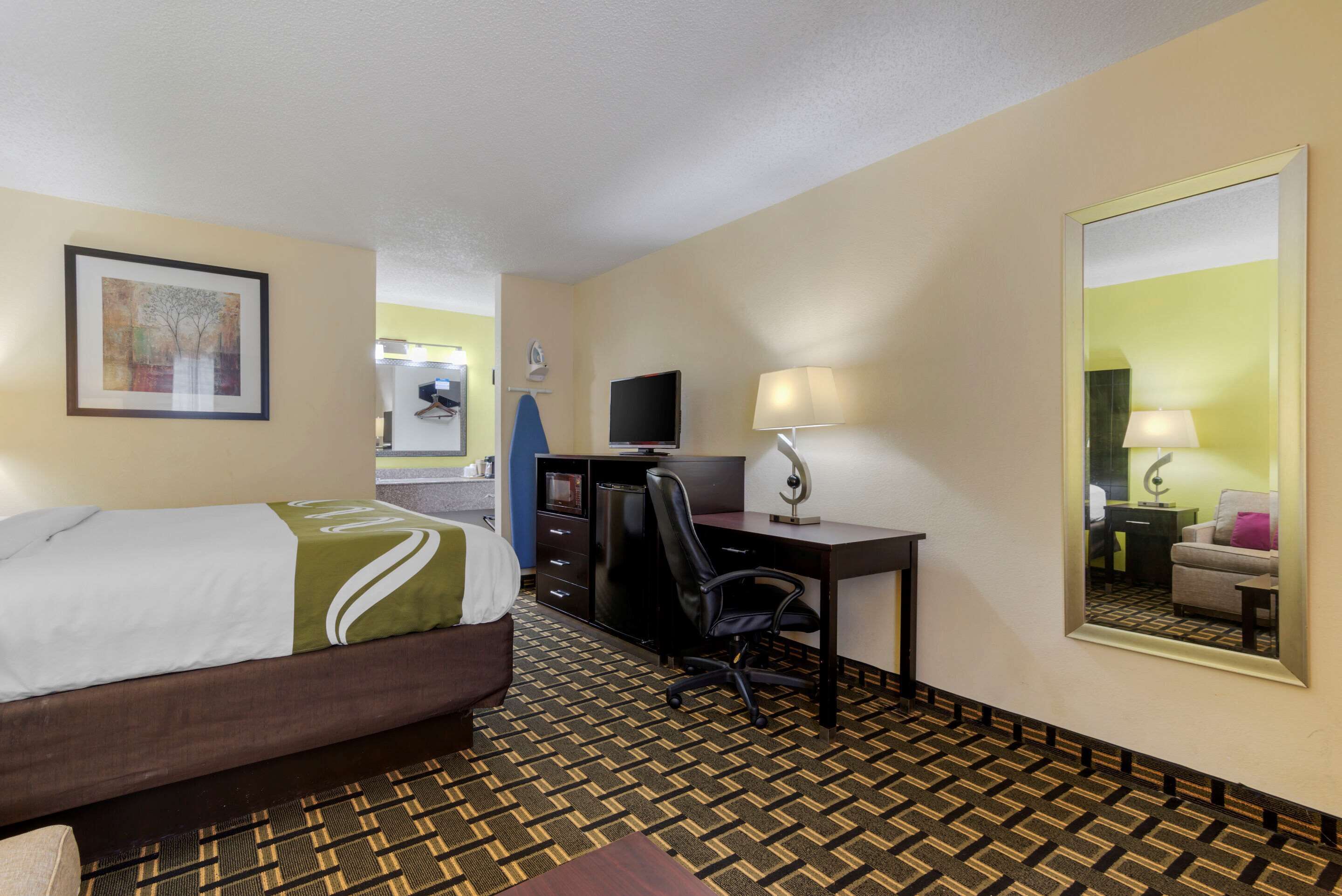 Una habitación de hotel con cama, escritorio, silla y un espejo grande.