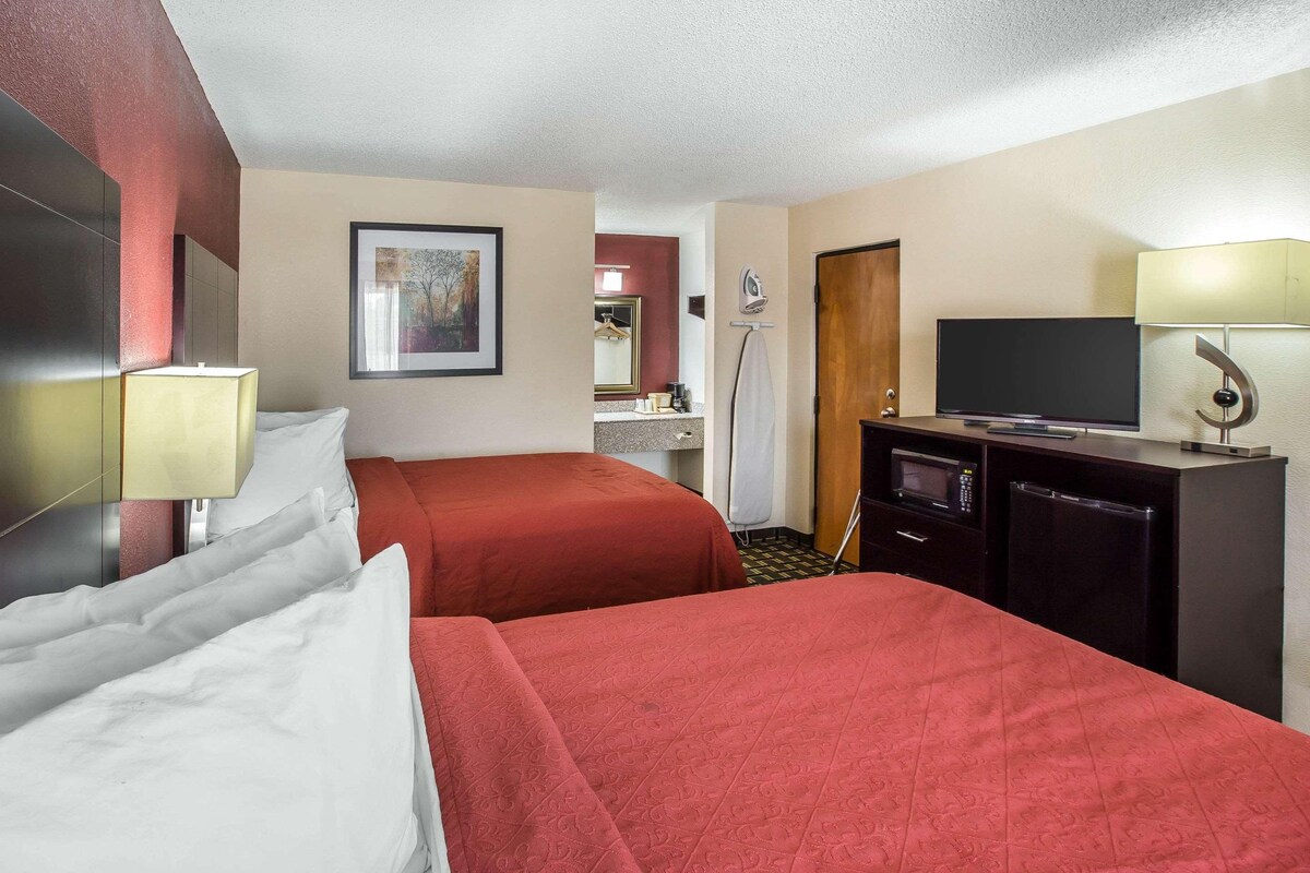 A hotel room with two beds, a television, a desk with a lamp, and a microwave.