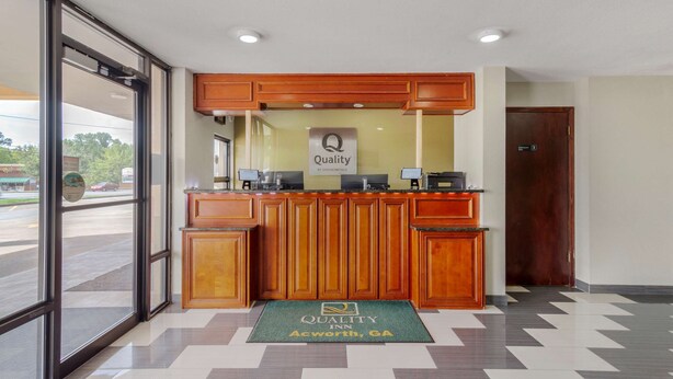 A reception desk with a 'Quality' sign, a check-in counter, and a green doormat with the hotel name. - Quality Inn Acworth North (Acworth)
