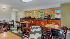 A hotel dining area with wooden tables and chairs, a kitchen counter with appliances, and pendant lighting. - Quality Inn Acworth North (Acworth)