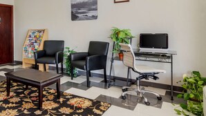 A reception area with a desk, two black chairs, a small table, a bulletin board, a potted plant, and a framed picture on the wall. - Quality Inn Acworth North (Acworth)