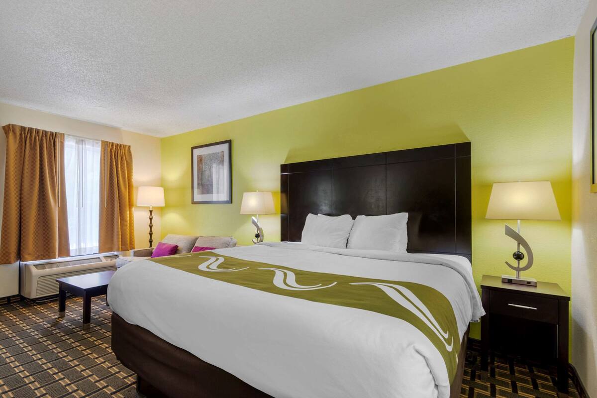 Habitación de hotel con una cama grande, dos mesitas de noche con lámparas, una ventana con cortinas y un cuadro colgado en la pared.
