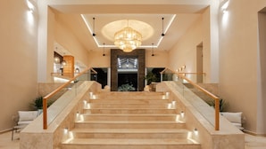 A grand staircase with marble steps and glass railings, leading to a well-lit entrance with a chandelier.