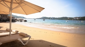 A beach with a lounge chair and umbrella, a sandy shore, and a calm sea with boats.