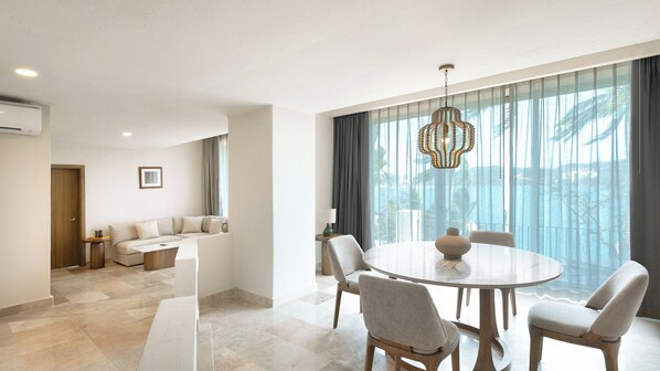 A modern hotel room with a dining area, a sofa, and a view of the sea.