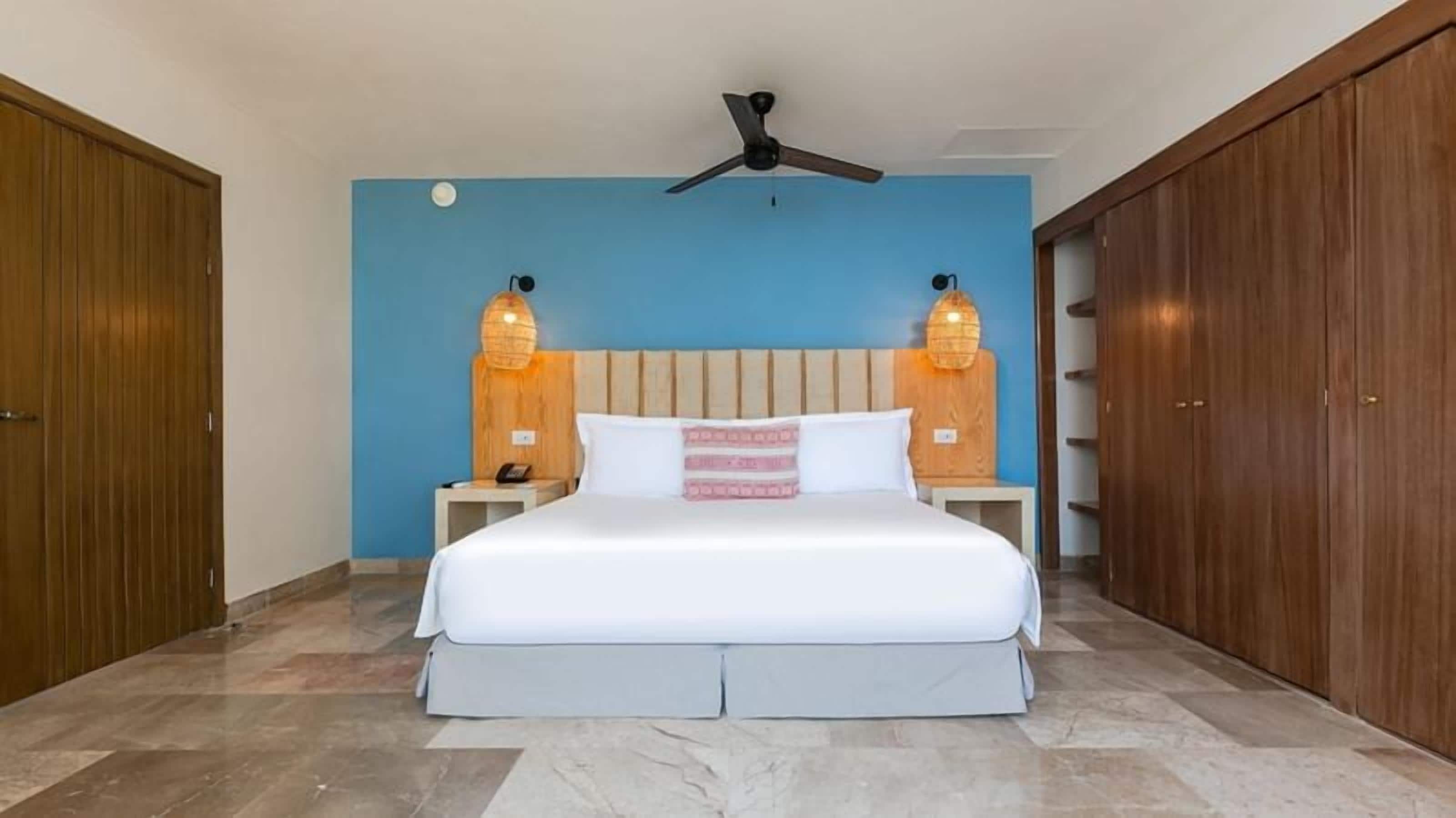A bedroom with a bed, a nightstand, a ceiling fan, and wooden wardrobes.
