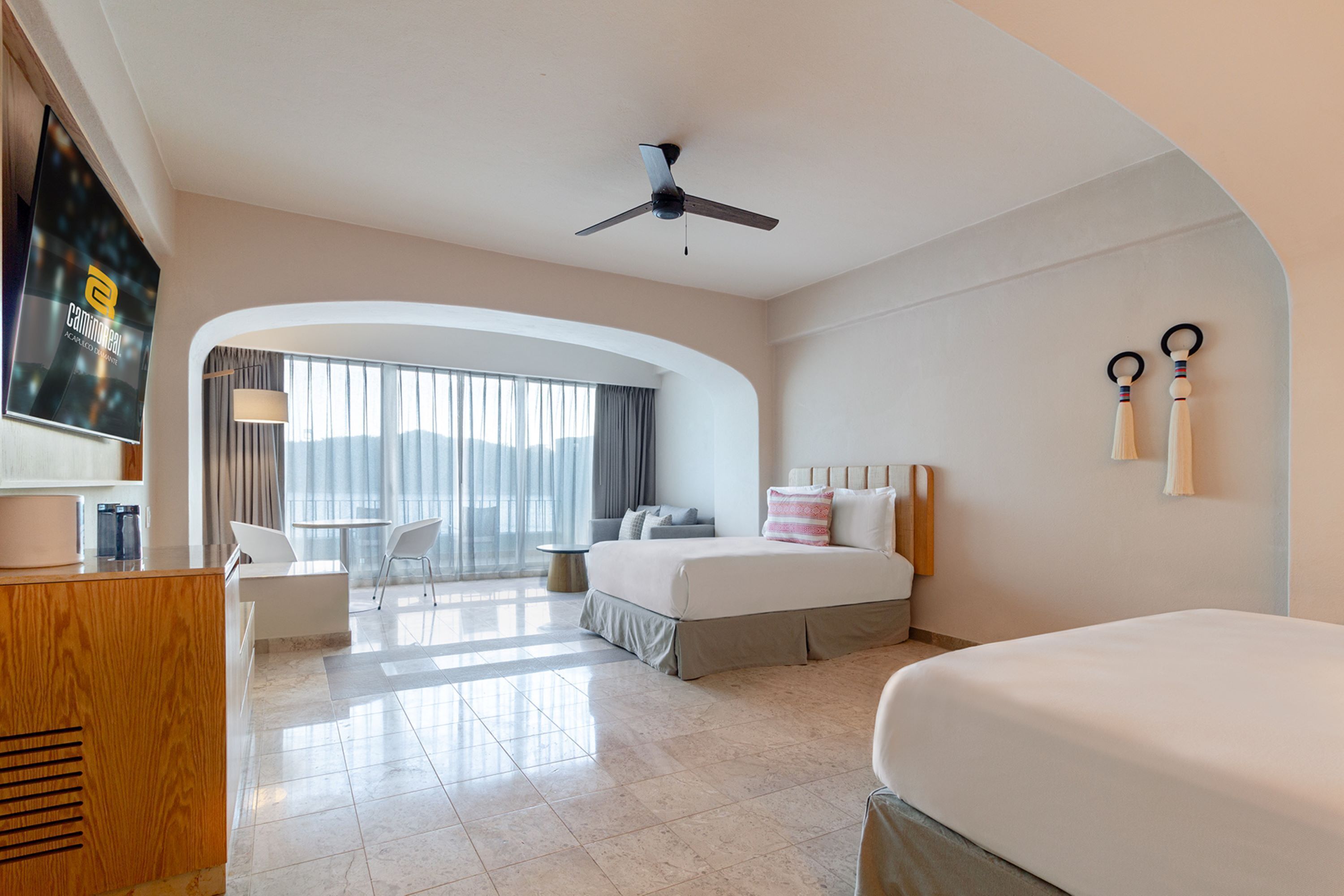 Una habitación de hotel con cama, escritorio, silla, televisión y ventilador de techo.