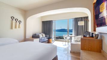 Quarto de hotel moderno com uma cama grande, um sofá, um espaço de refeições e vista para o mar.