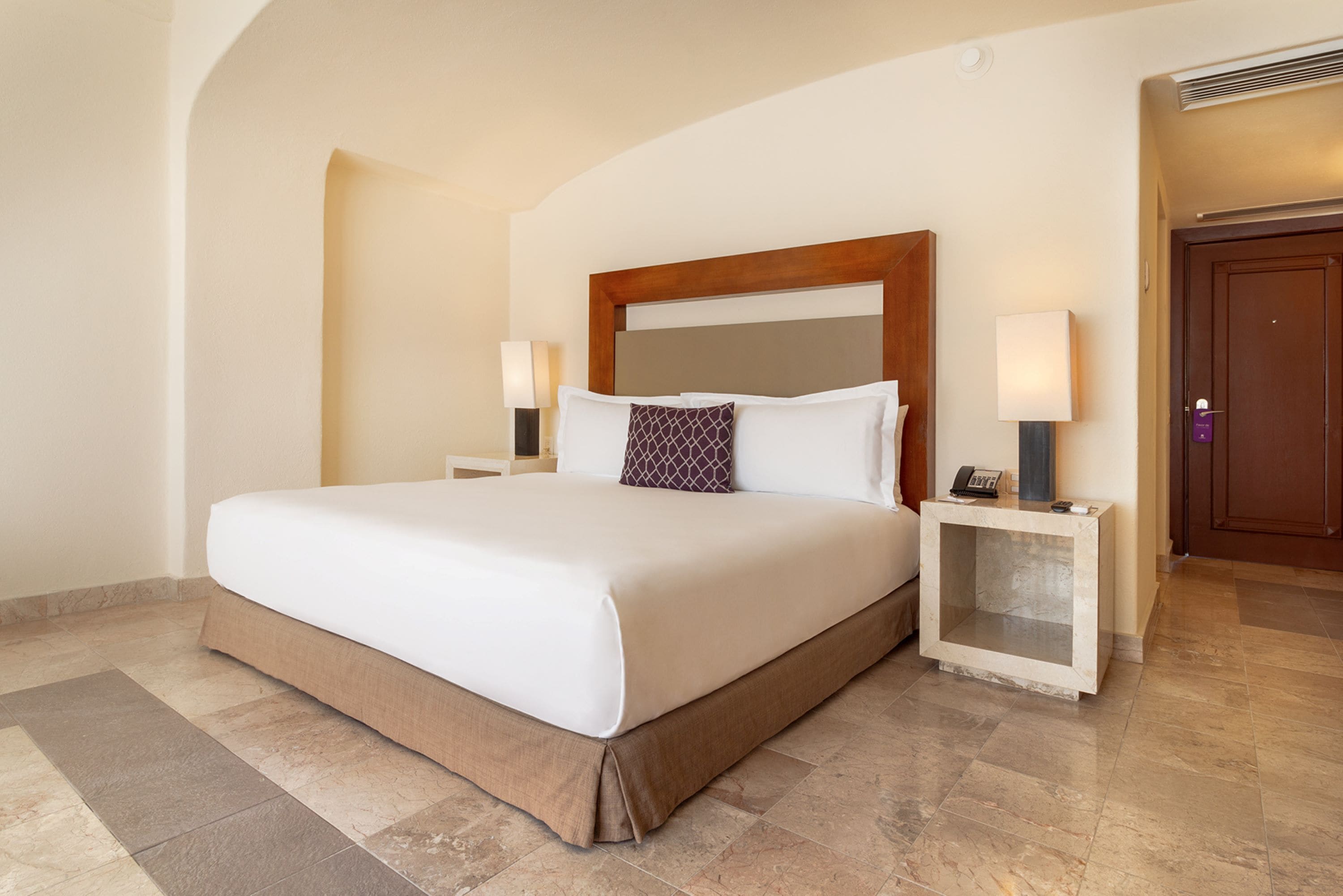 Habitación de hotel con una cama grande, dos mesitas de noche, una mesilla auxiliar, un cabecero de madera y una puerta.