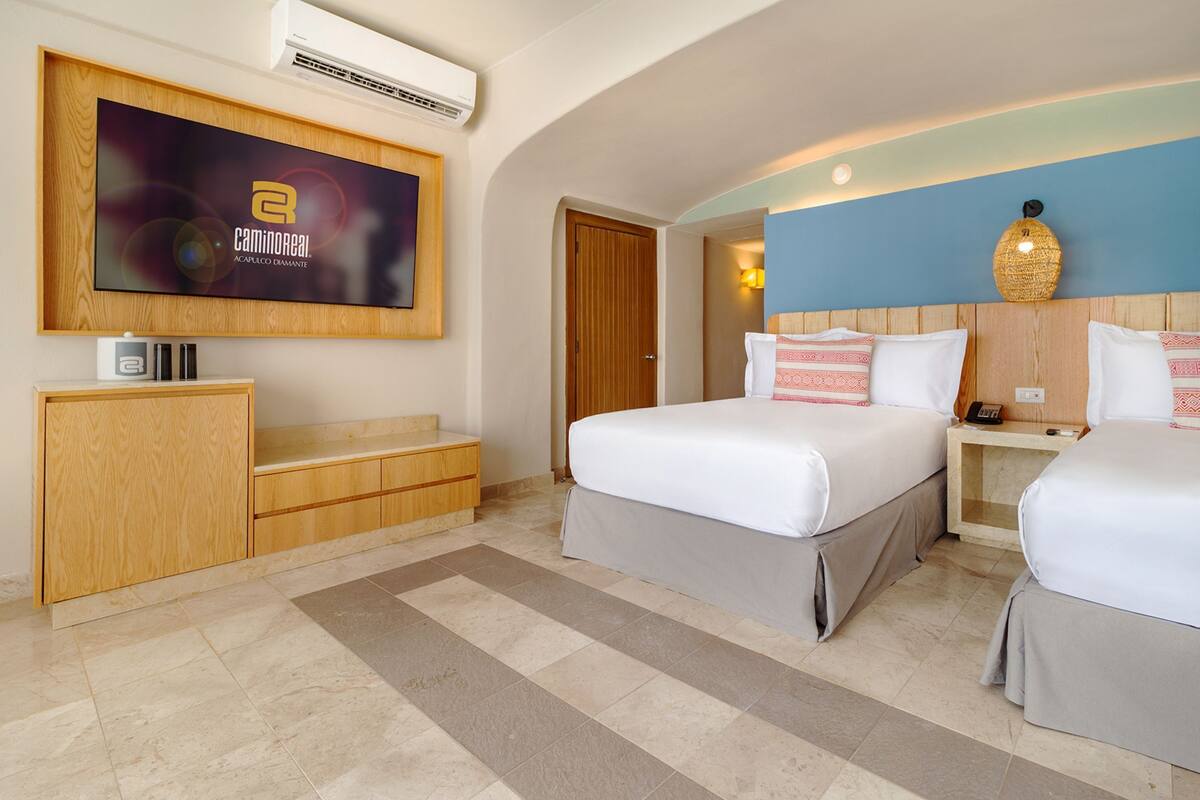 A hotel room with two beds, a TV mounted on the wall, a wooden cabinet, and a tiled floor.