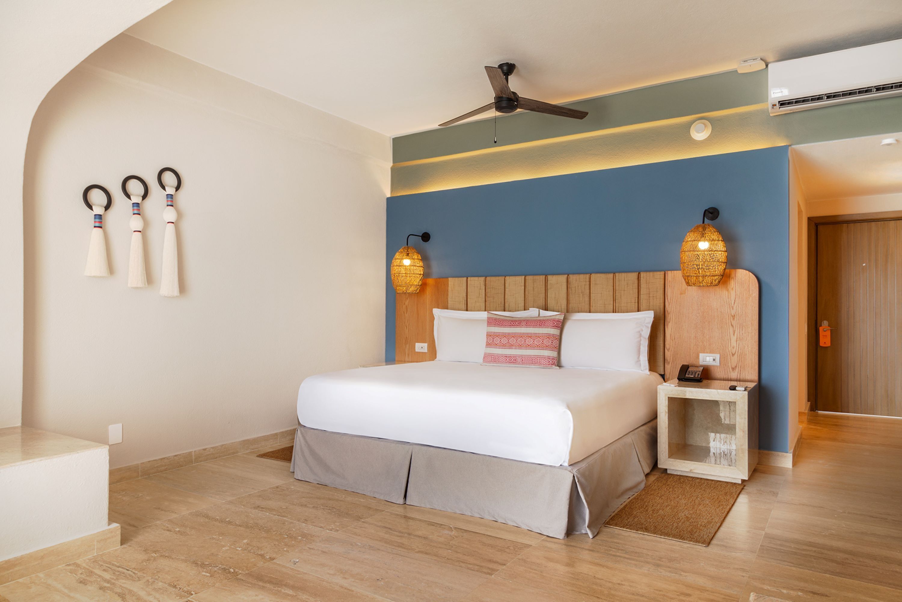 A bedroom with a bed, bedside tables, a ceiling fan, wall-mounted lamps, and a wooden headboard.