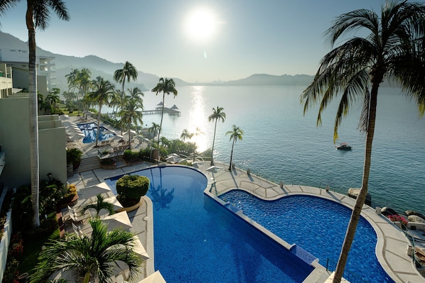 Una piscina con vistas al mar, rodeada de palmeras y un edificio con zona de piscina.