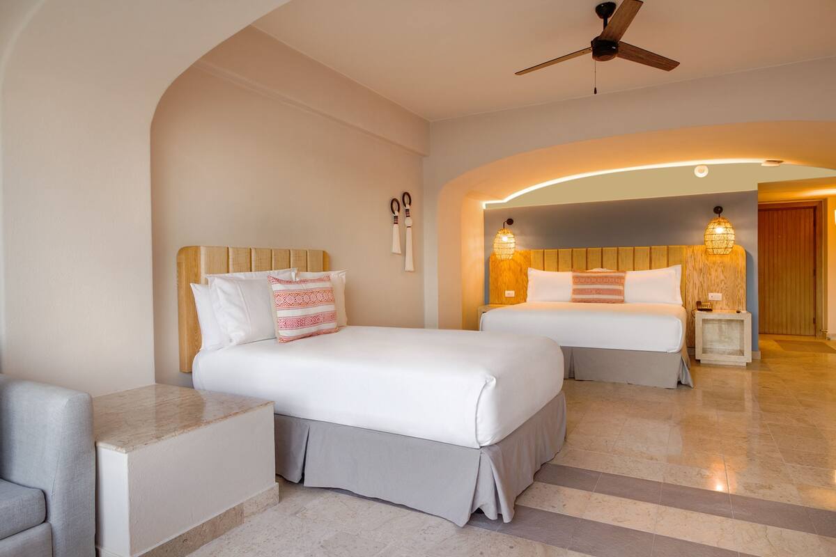 A hotel room with two beds, a sitting area, and a ceiling fan.