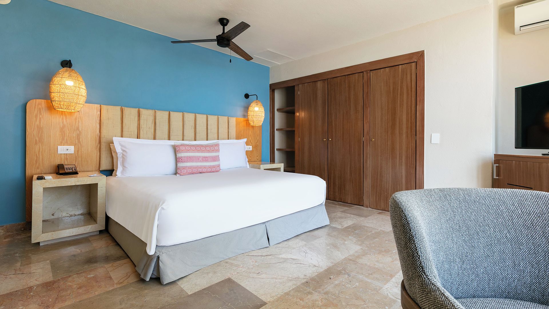 A hotel room with a bed, bedside tables, a ceiling fan, a wardrobe, and a television.