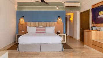 A modern hotel room with a large bed, wooden headboard, two bedside lamps, a ceiling fan, and a TV on the wall.