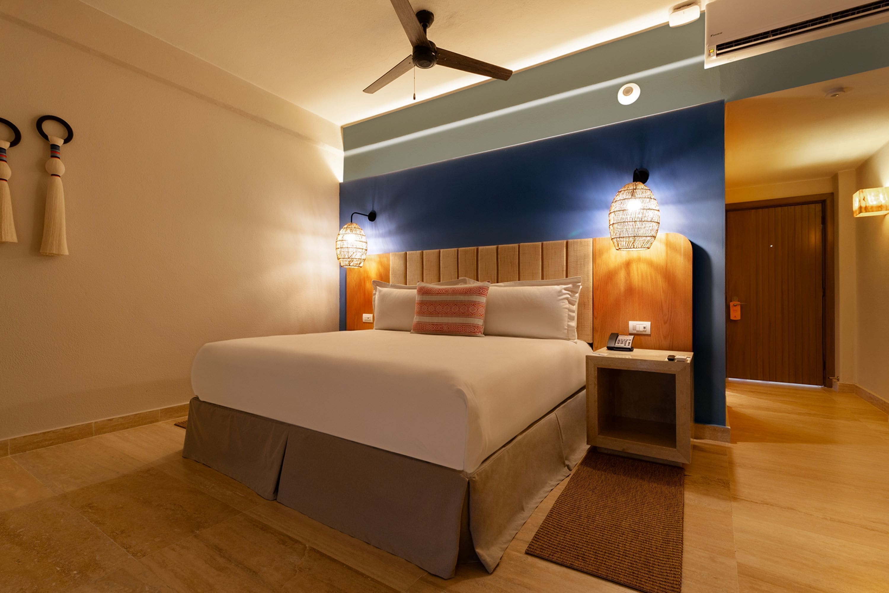 A modern hotel room with a large bed, a ceiling fan, and two wall-mounted lamps.