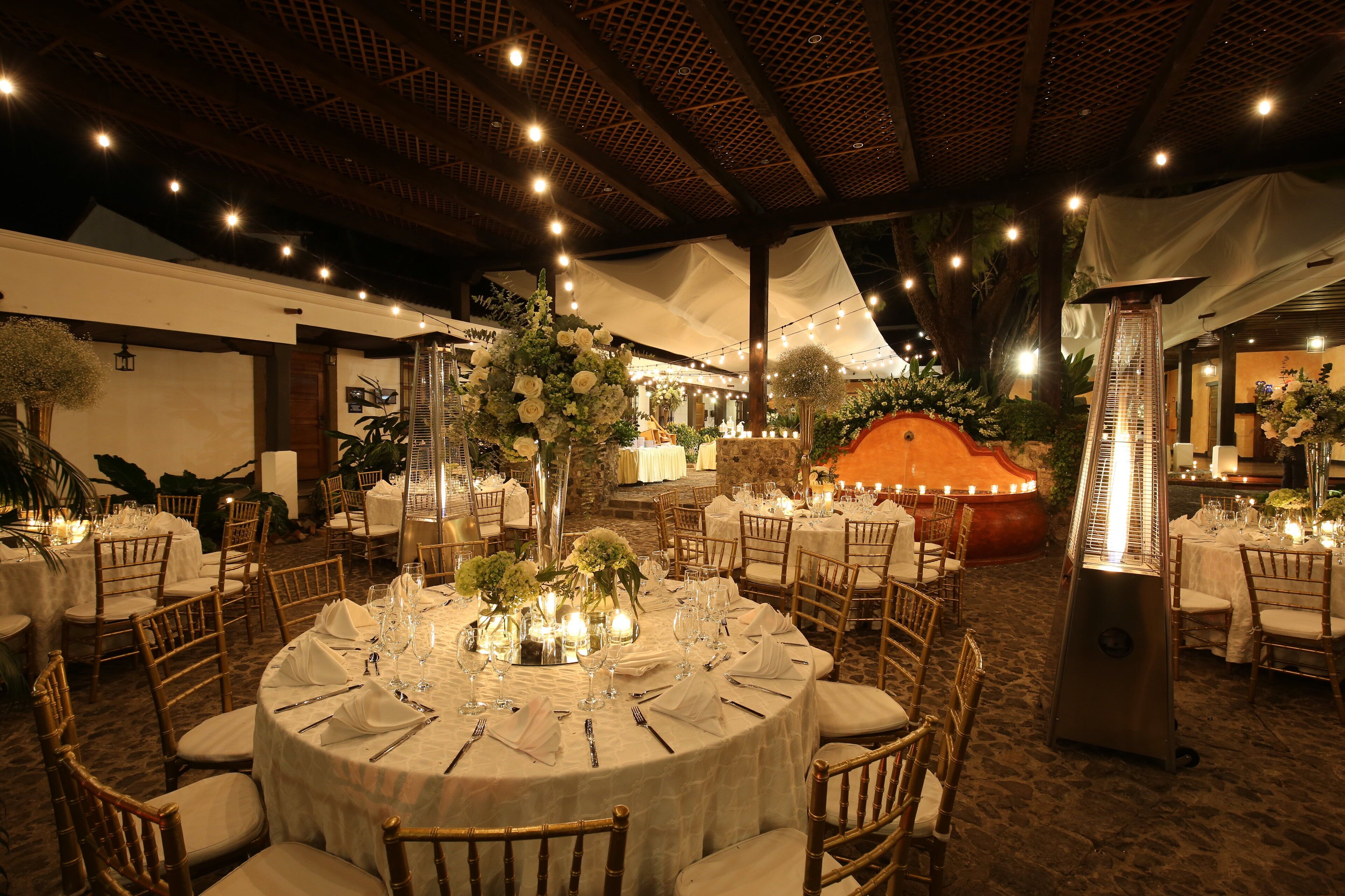 A banquet hall with round tables set for a formal event, featuring white tablecloths, floral centerpieces, and candle lighting.