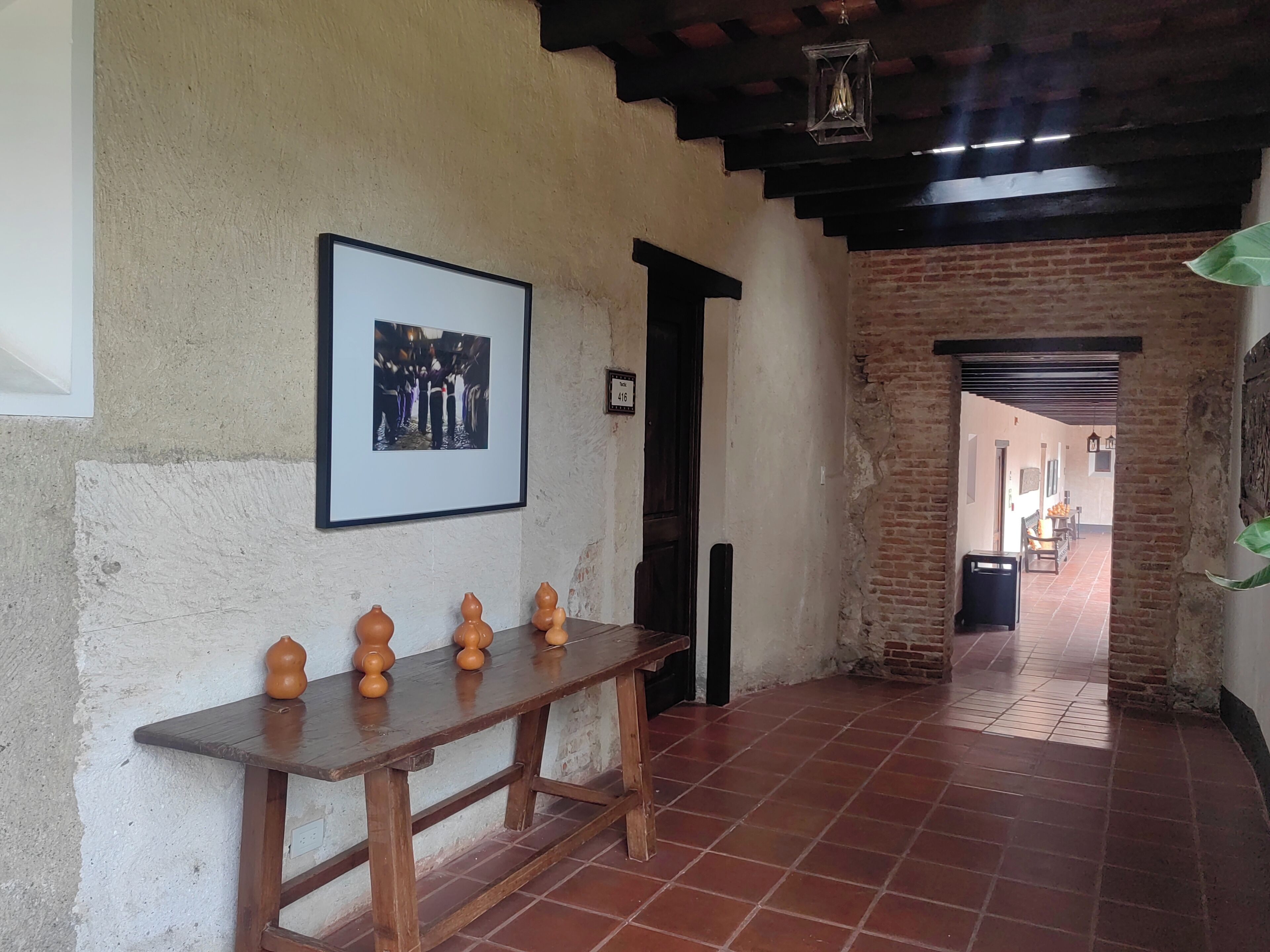 A hallway with a wooden bench, a framed photo on the wall, and a brick wall.
