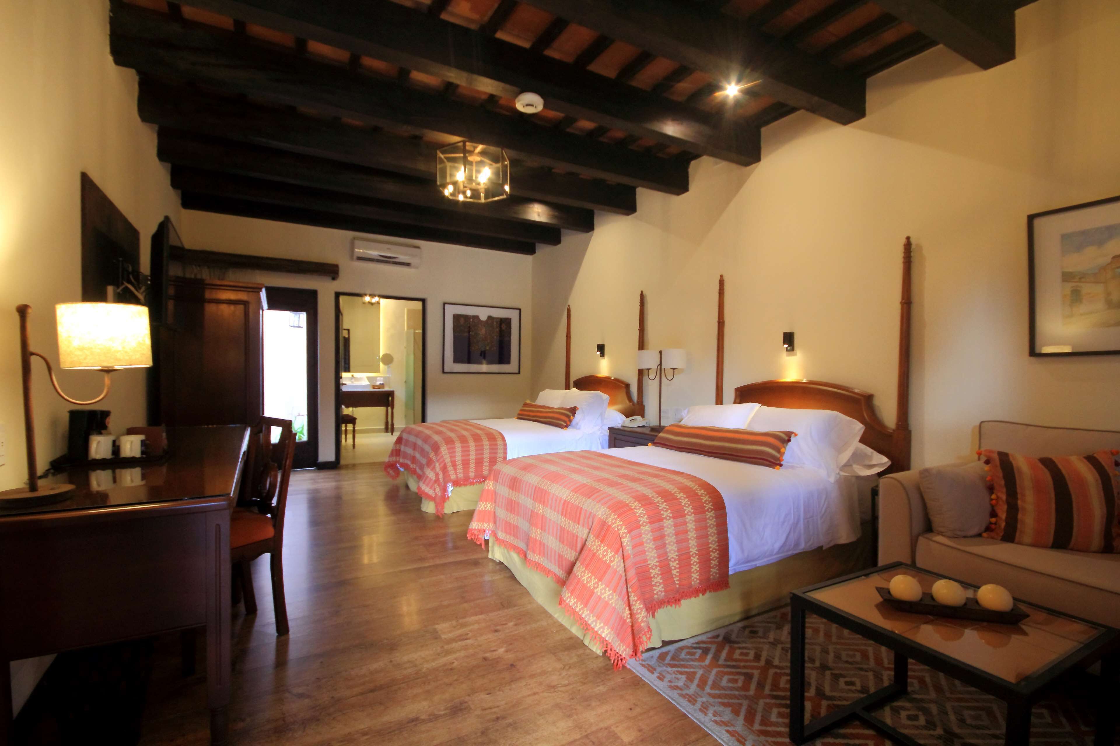 A hotel room with two beds, a desk, a chair, a sofa, and a coffee table.