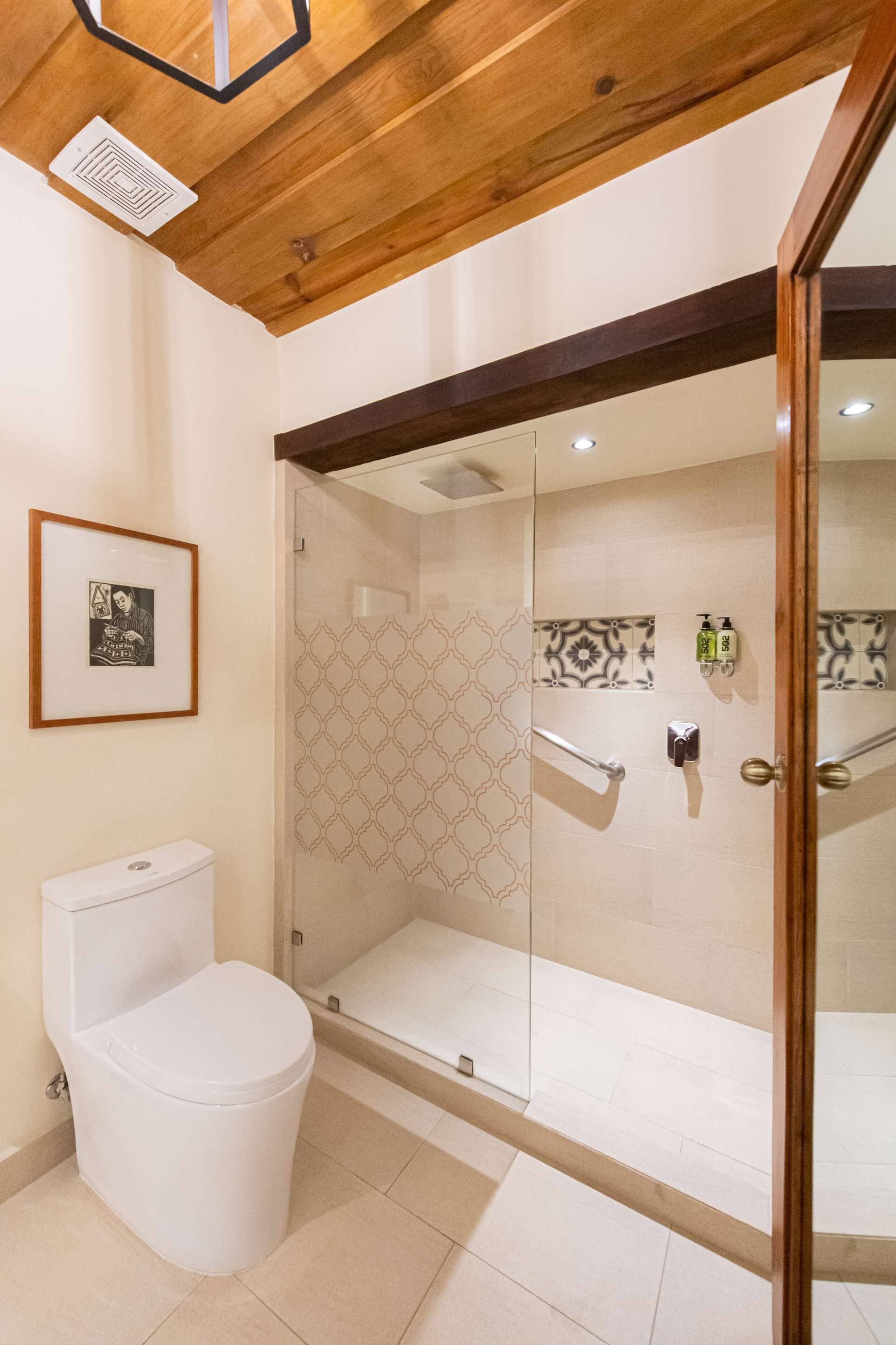 Un baño moderno con cabina de ducha de vidrio, inodoro blanco y un cuadro en la pared.