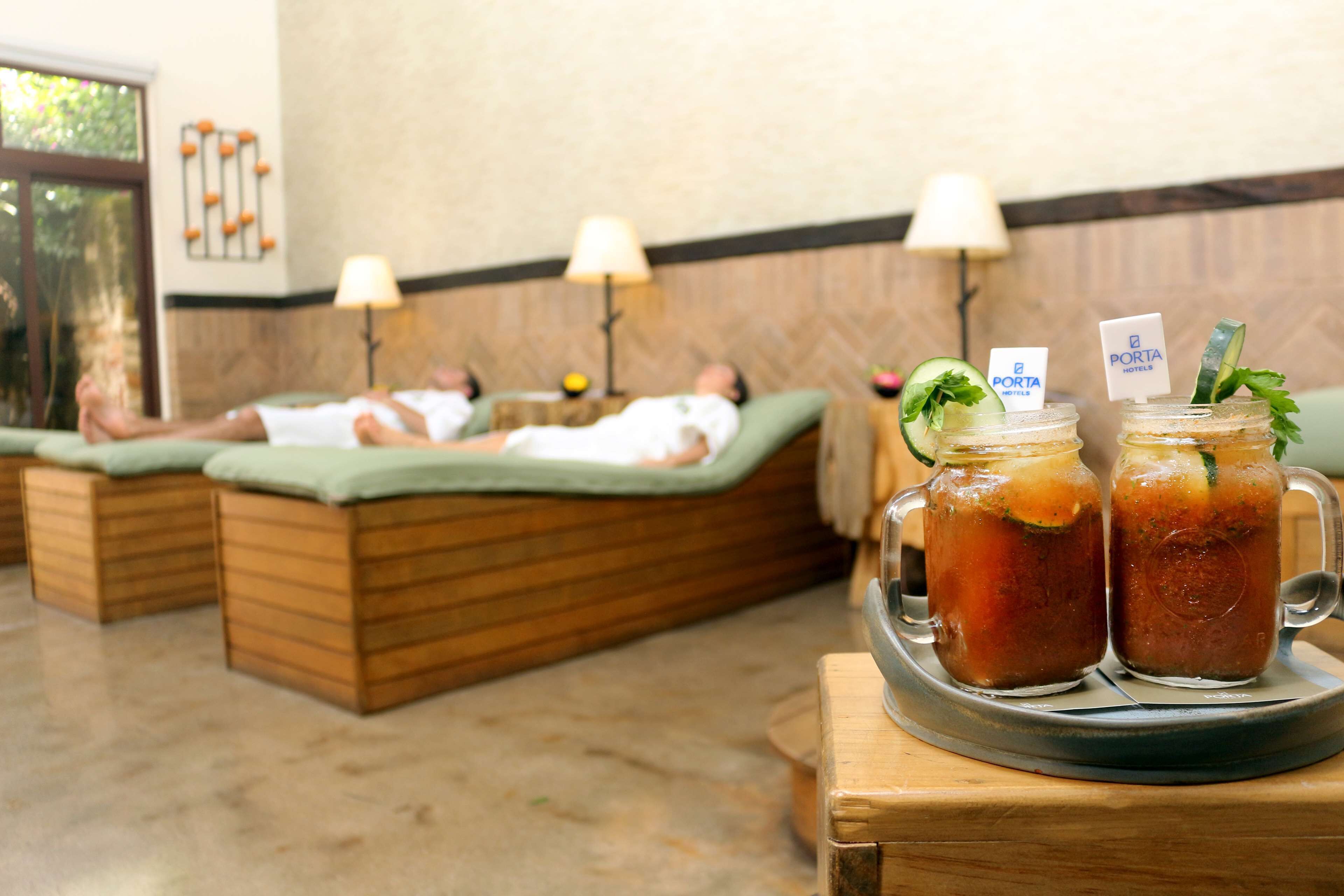Un espacio de spa con sillones de madera, una bandeja con dos vasos de té helado y un letrero que dice 'Porta Hotels'.