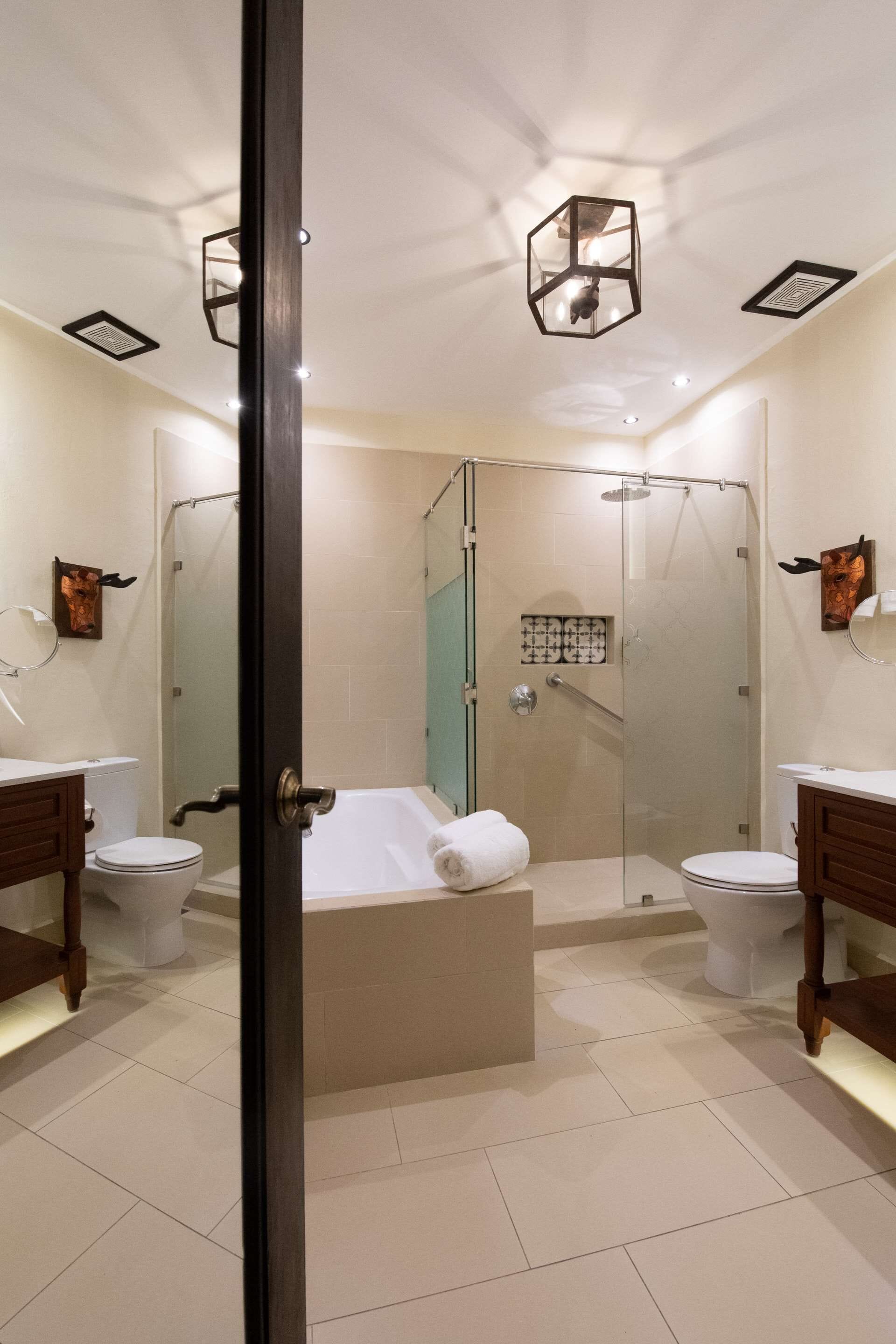 A modern bathroom with a glass-enclosed shower, a bathtub, and two toilets.