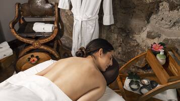 Ein Spa-Raum mit Massagetisch, Holzmöbeln, einer Steinwand und einer Ablage mit Wellnessprodukten.