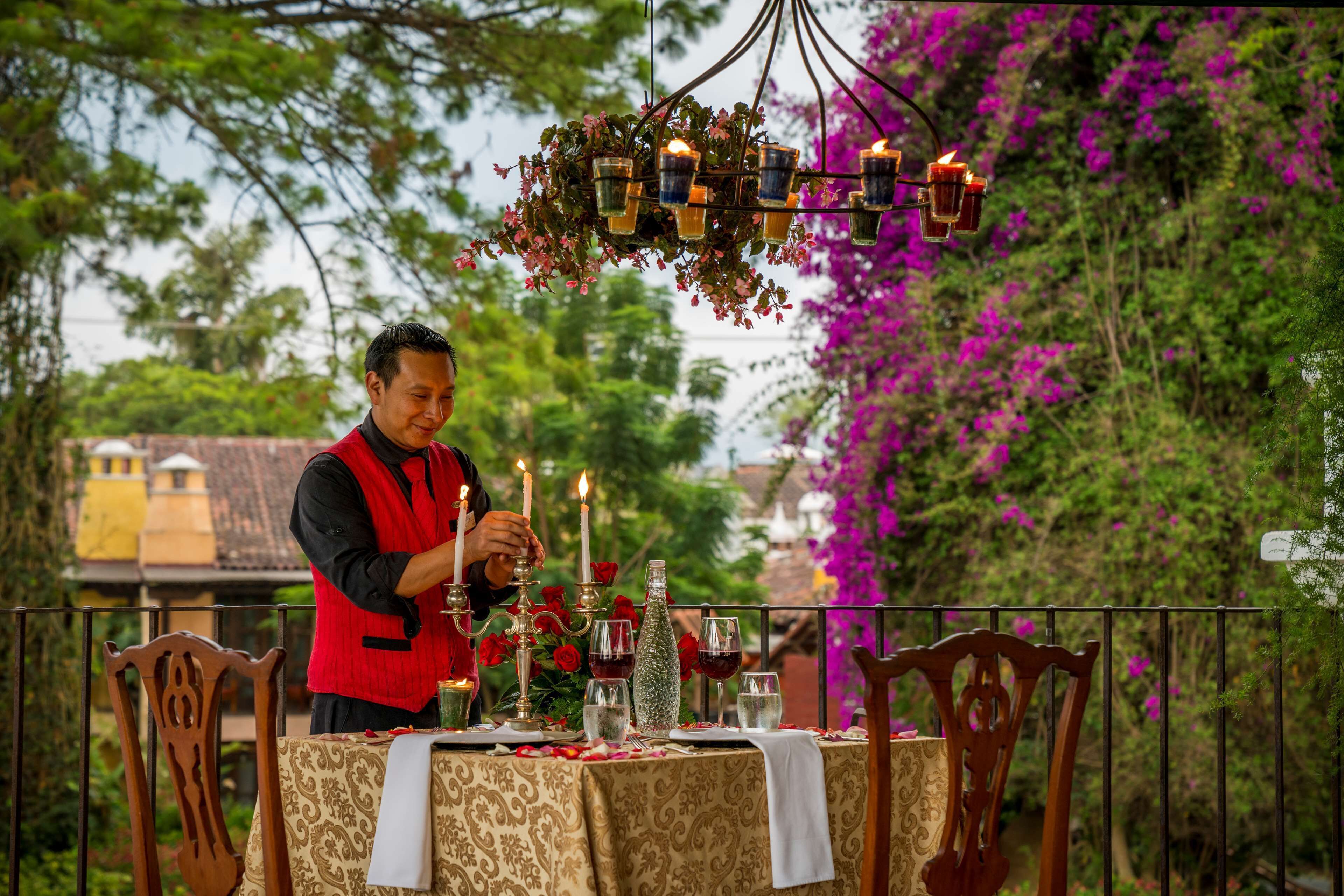Mesa al aire libre decorada con velas, flores y una persona ordenando la mesa.