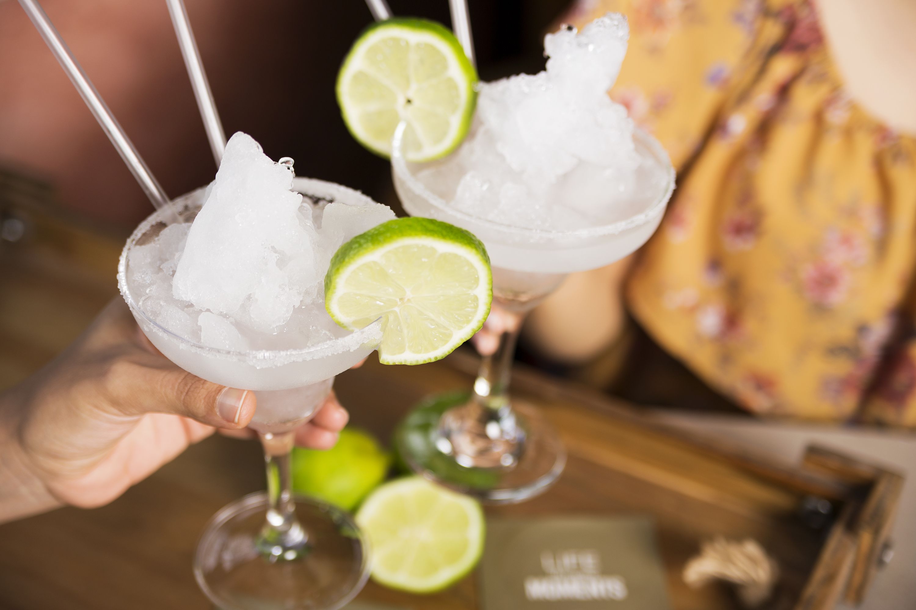 A person holding a cocktail glass with ice and a lime slice.