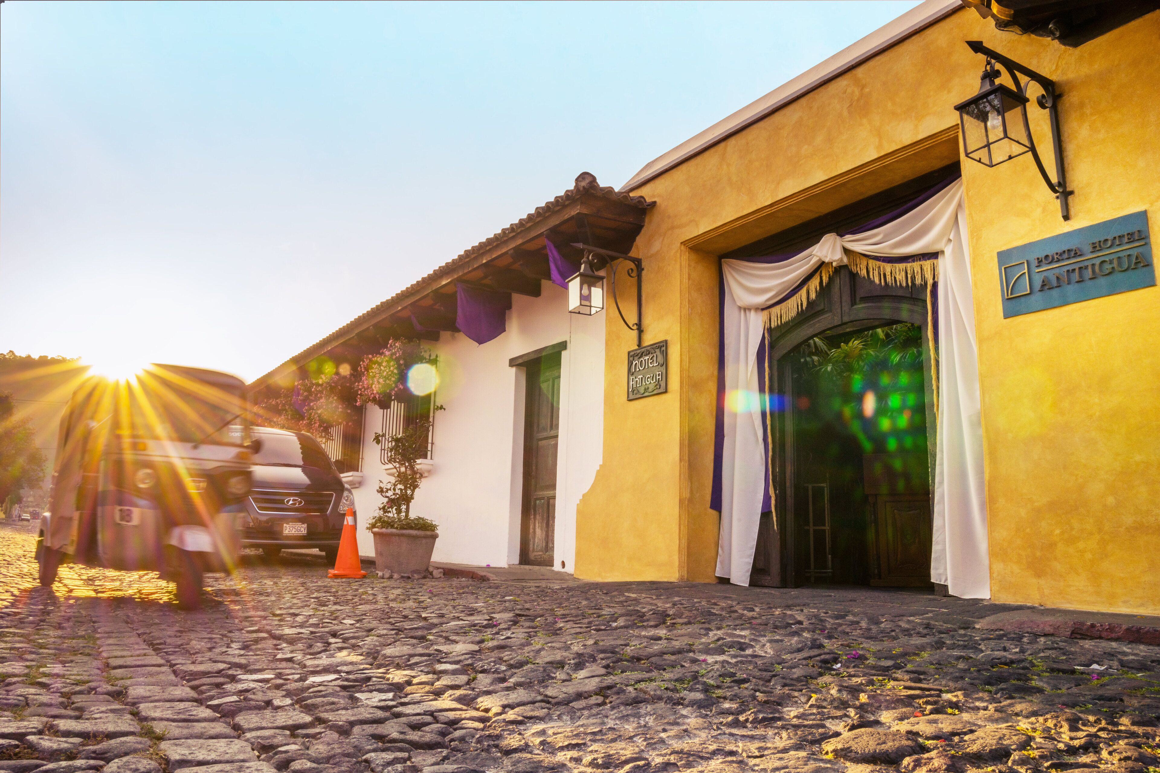 A cobblestone street leading to a building with a sign reading "Hotel Antigua."