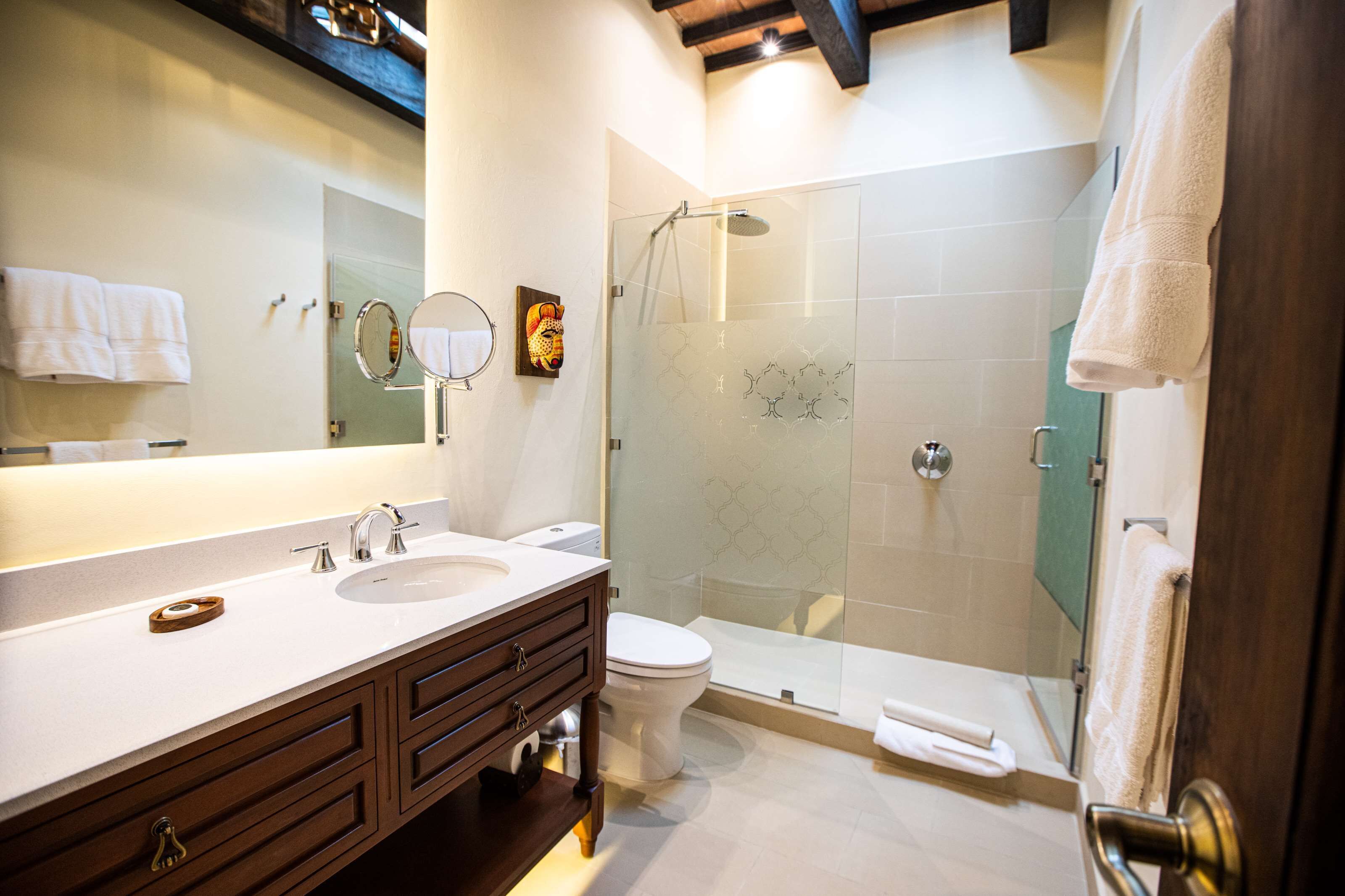 A modern bathroom with a double sink vanity, a toilet, a glass-enclosed shower, and a large mirror.