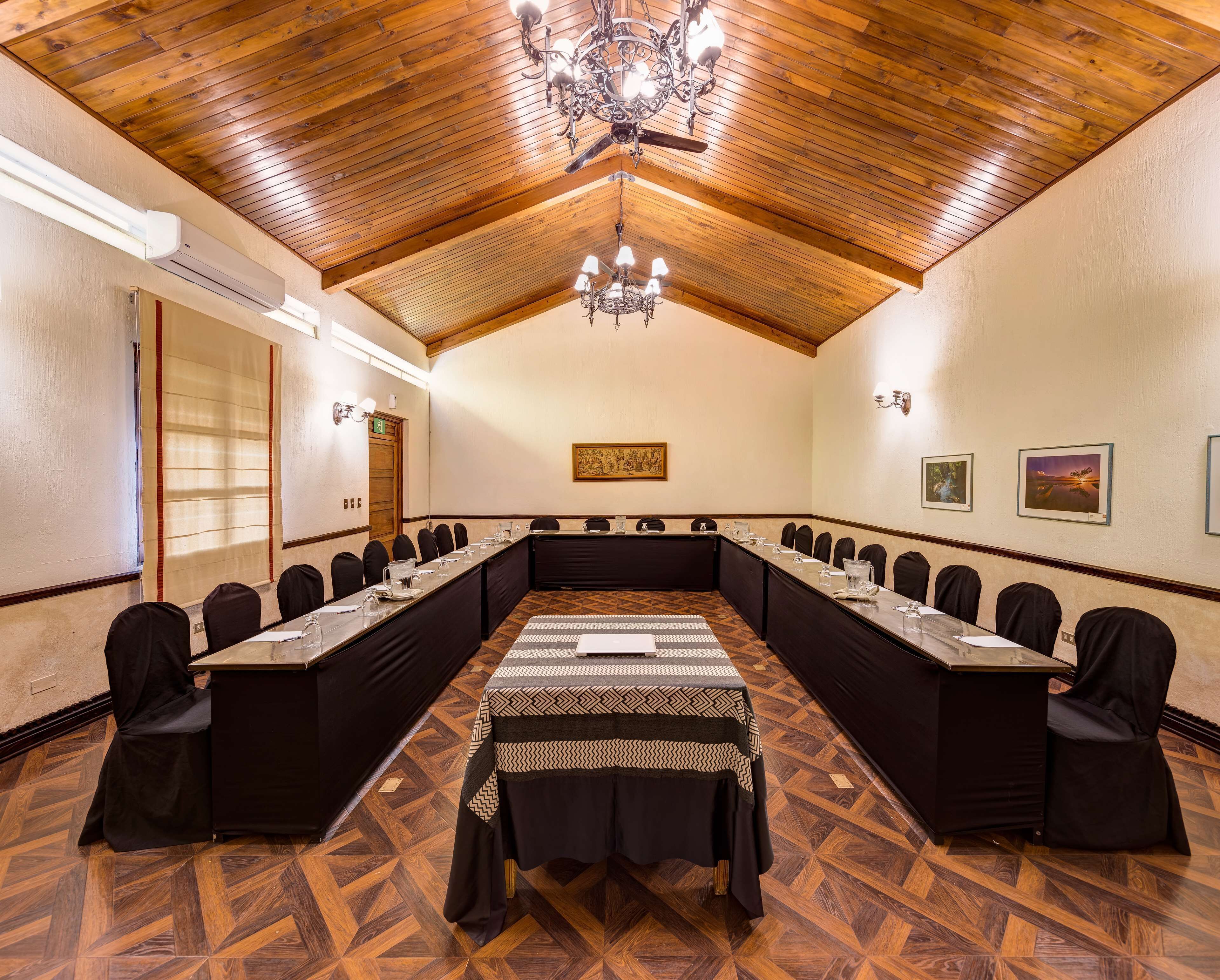 Un salón de conferencias con una larga mesa, sillas, una araña y suelo de madera.