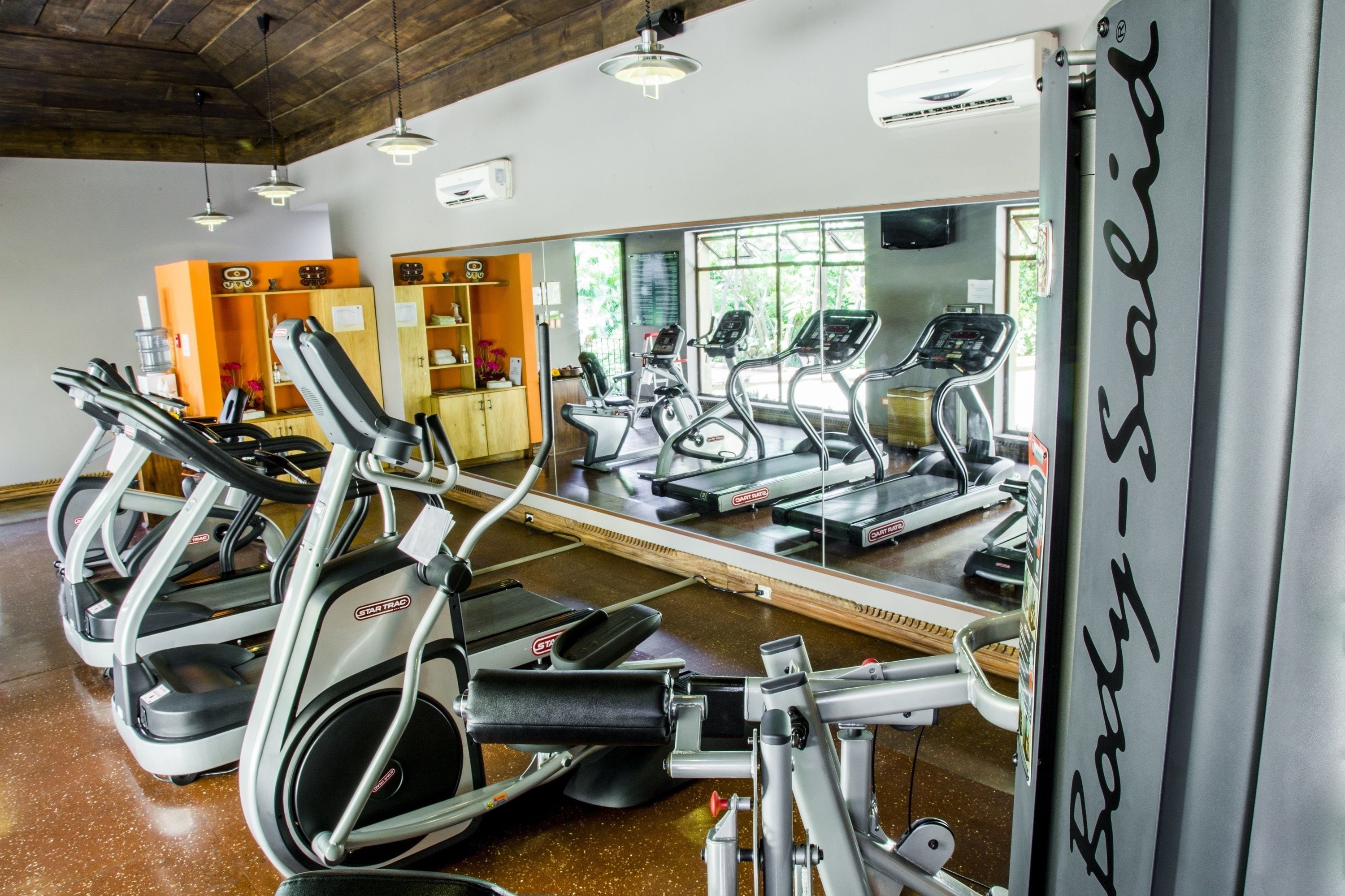 Un gimnasio con cintas de correr, bicicletas estáticas y un espejo grande.