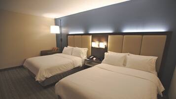 A hotel room with two beds, a nightstand, a lamp, and a wall-mounted light fixture.
