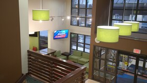 En hotellobby med en trappa, gröna sittmöbler, en tv-skärm som visar ordet ”HÖGER” och stora fönster.