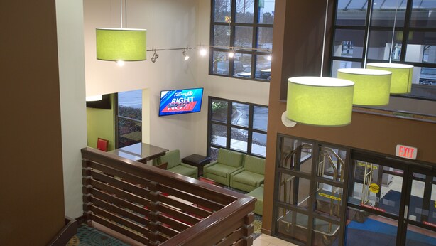 A hotel lobby with a staircase, green seating, a TV displaying 'RIGHT' on the screen, and large windows. - Holiday Inn Express Anderson by IHG (Anderson)