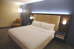 A hotel room with a large bed, two bedside tables with lamps, a chair, and a nightstand with a clock.