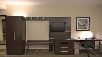 A hotel room with a desk, chair, wardrobe, and a television.