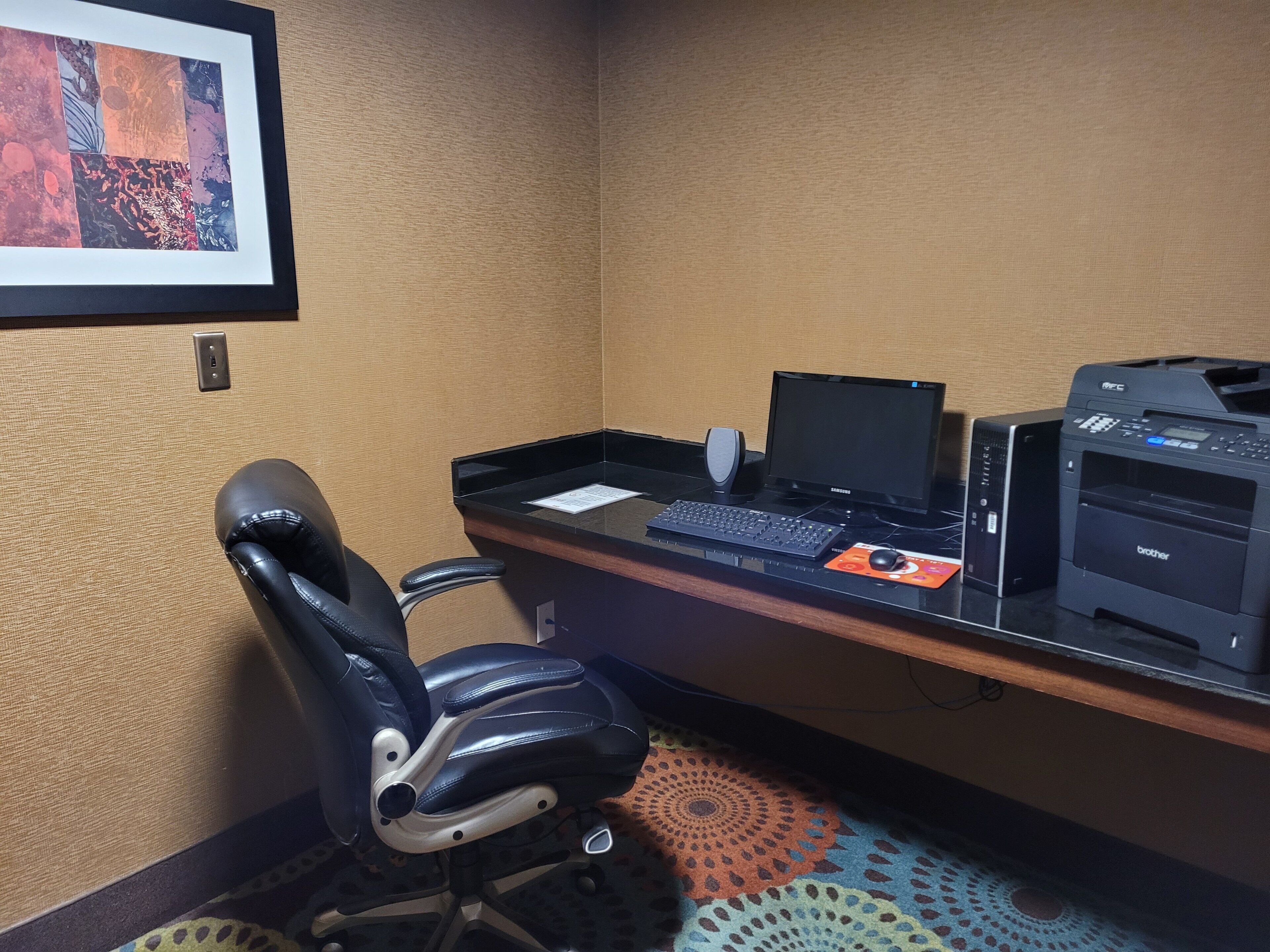 Una oficina de hotel con escritorio, computadora, impresora y una silla.