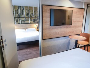 Une chambre d’hôtel avec un lit, un téléviseur fixé au mur, une petite table ronde et une chaise.